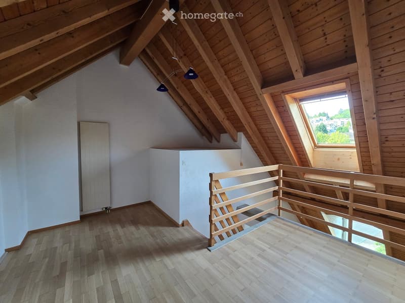 Empty attic space with wooden beams, wooden flooring, and a skylight window offering a view of the outside. The room features a wooden railing and a small built-in closet.