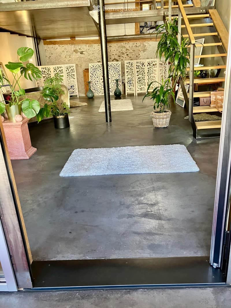 Modern, open-plan living space with concrete floors, decorative screens, potted plants, and a staircase leading to an upper level.
