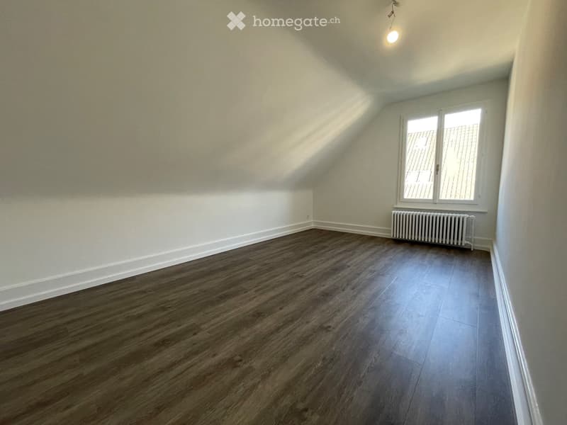 Empty room with wooden flooring, white walls, a window with white frame, and a radiator below the window.