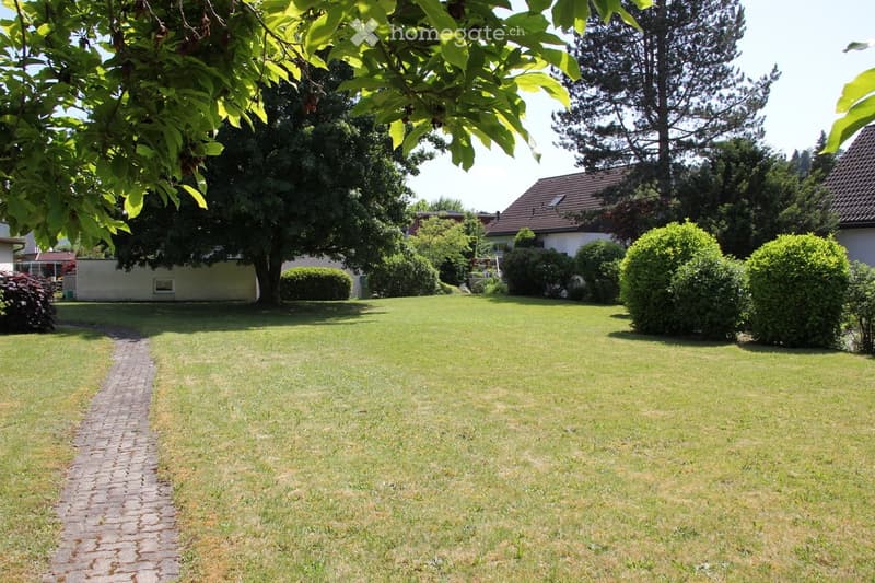 Well-maintained lawn with trimmed hedges, a brick pathway, and surrounding trees, with a house visible in the background.