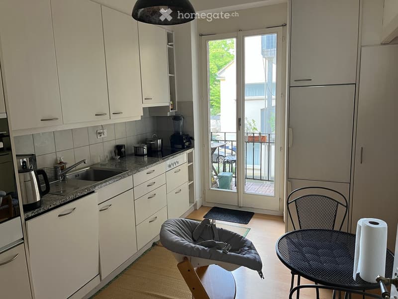 Modern kitchen with white cabinets, stainless steel appliances, and a small dining area with a table and chairs. A cat bed is placed near the dining area.