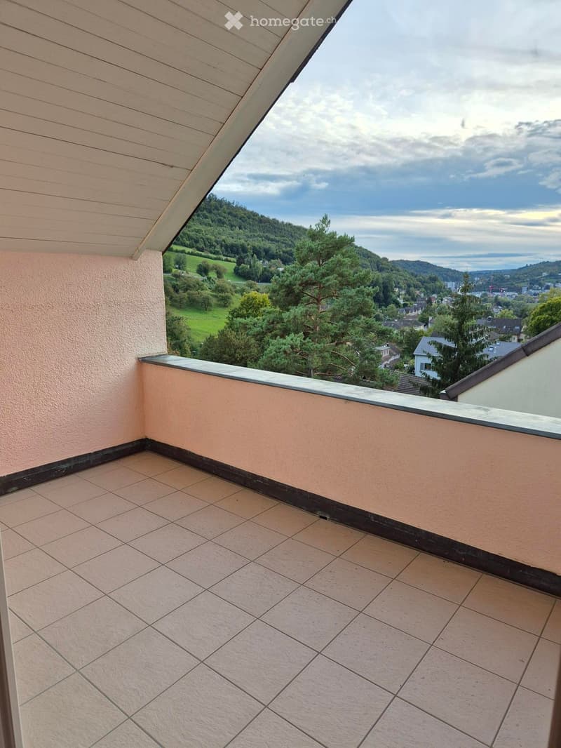 Balcony with tiled floor, beige walls, and a railing, offering a scenic view of a green landscape and town.