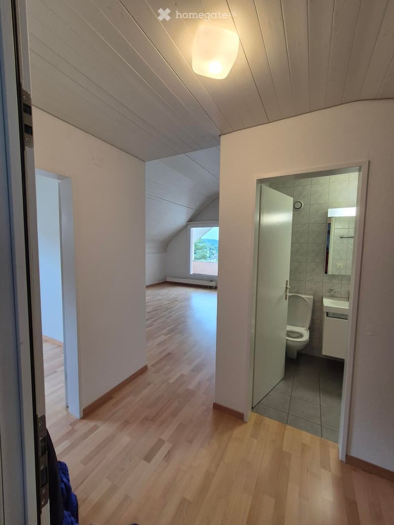 Empty hallway with wooden flooring, white walls, and a view of a small room and a bathroom through open doors.
