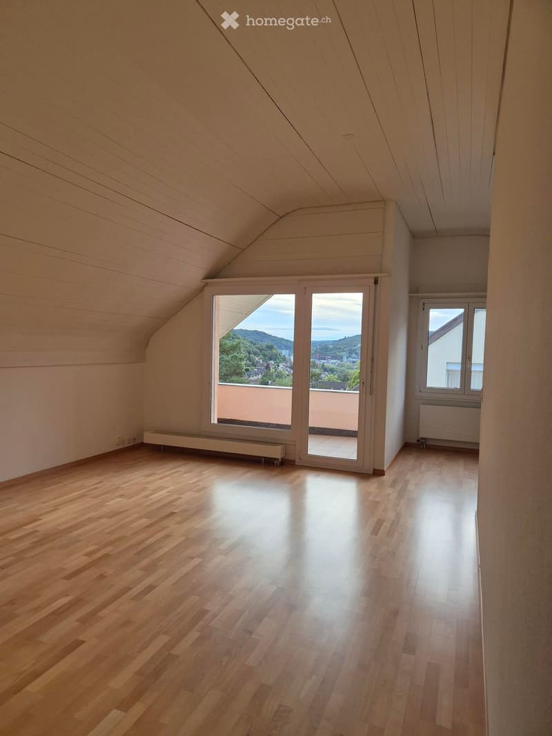 Empty attic room with wooden flooring, slanted wooden ceiling, large sliding glass door leading to a balcony, and a window on the side.