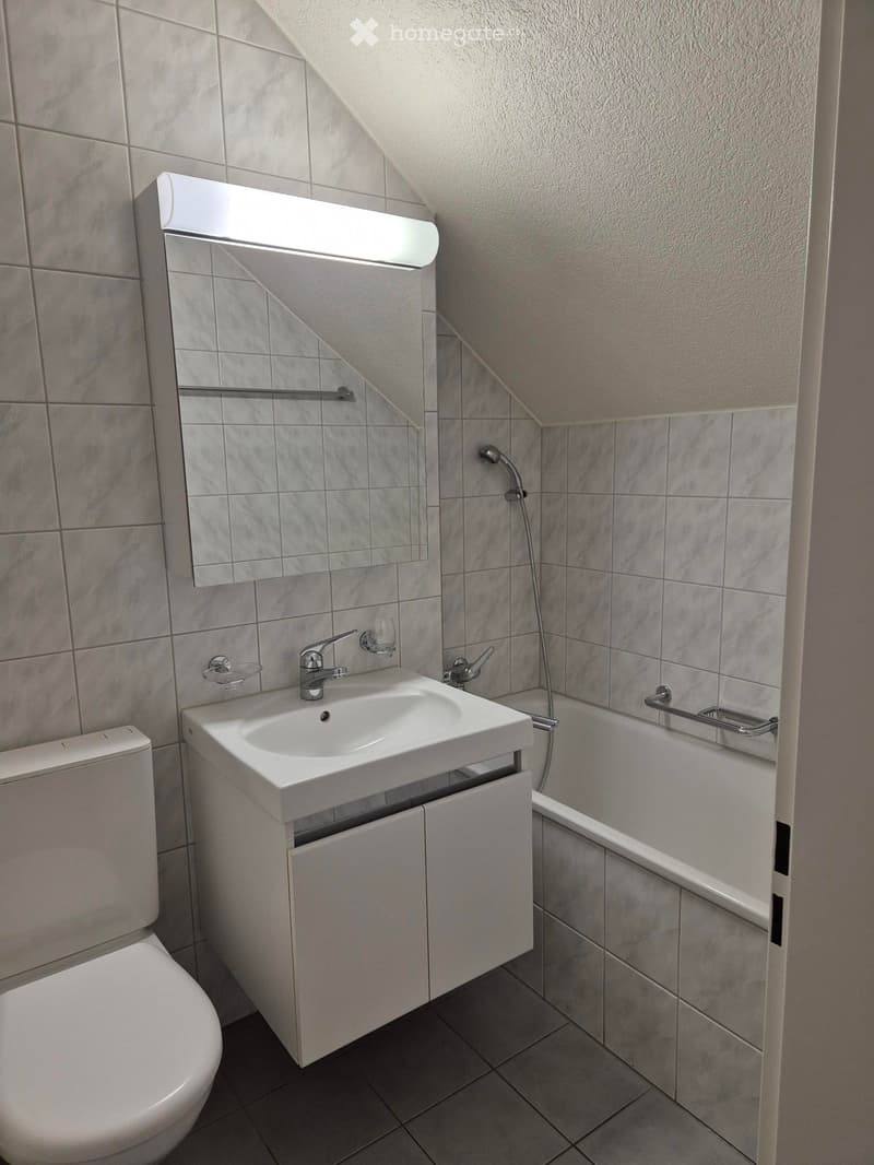 Modern bathroom with a white sink, toilet, bathtub, and mirror. Features tiled walls and a sleek design.