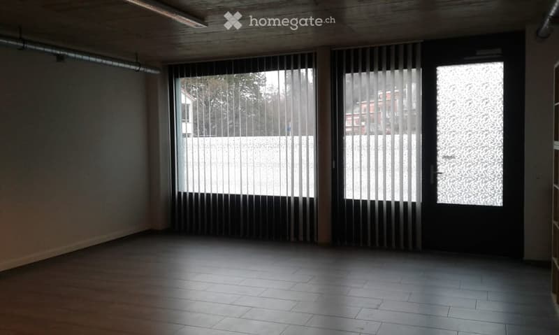 Empty room with wooden flooring, large windows with blinds, and a door leading outside.