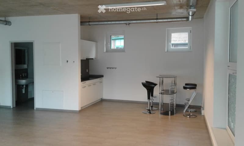small, square kitchen with white cupboards, wooden floor, three black bar stools, round table, sinks with faucets