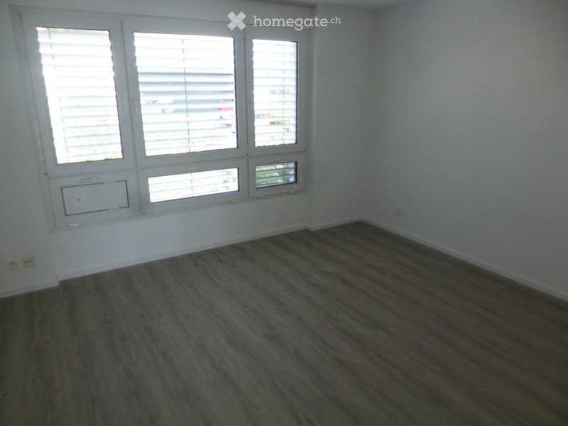 Empty room with wooden flooring and white walls, featuring multiple windows with blinds and an air conditioning unit on the wall.