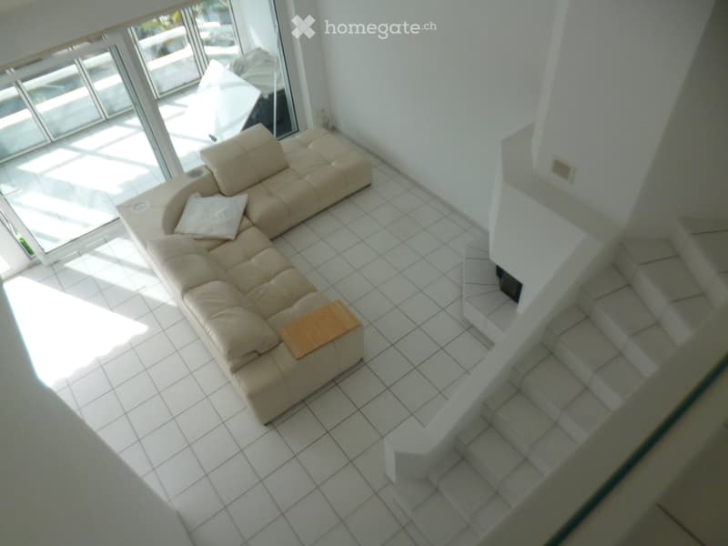 Living room with a beige sectional sofa, a small wooden table, and large windows letting in natural light.