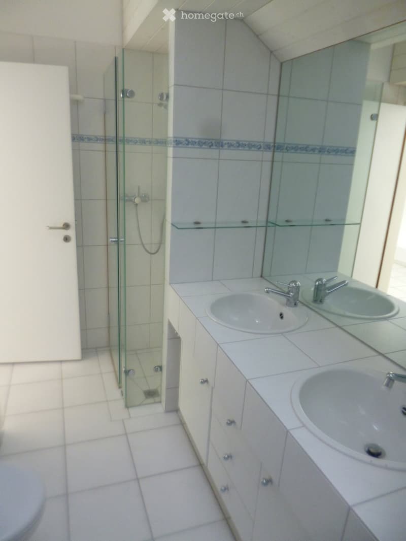 Modern bathroom with white tiles, two sinks, a large mirror, and a glass-enclosed shower area.