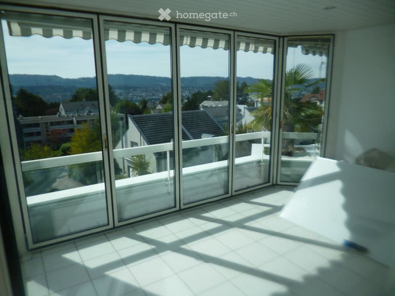 Bright, tiled balcony with large sliding glass doors offering a scenic view of the city and surrounding hills.