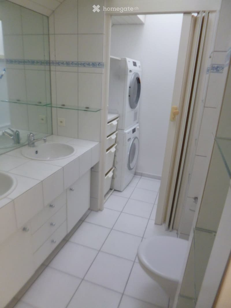 Bathroom with white tiled floor, sink with mirror, washing machine, and toilet.