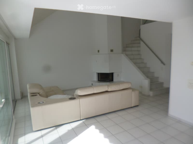 Modern living room with a white leather sofa, fireplace, and staircase leading to an upper level.