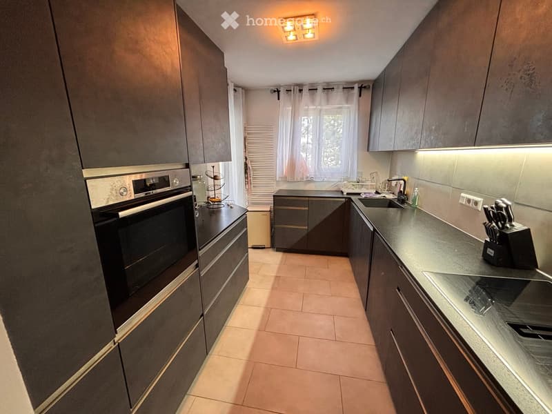 Modern kitchen with dark grey cabinets, stainless steel oven, granite countertop, and built-in lighting.