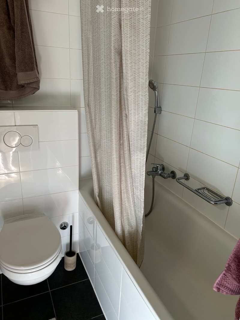 Bathroom with a toilet, bathtub, shower curtain, and a towel hanging on the side.
