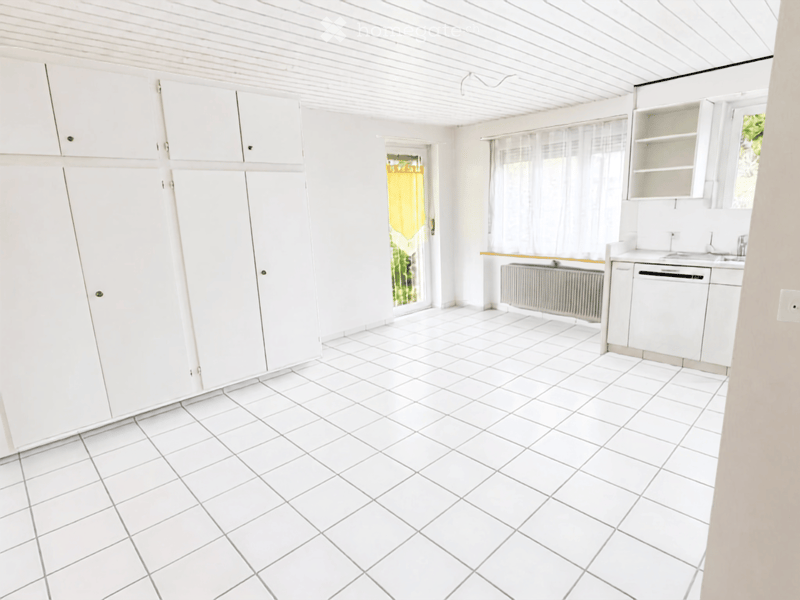 Empty kitchen with white tiled floor, white cabinets, and a sink area. No furniture or appliances are present.