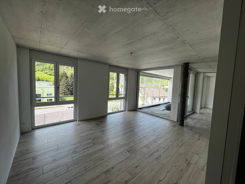 Empty room with wooden flooring, large windows, and a concrete ceiling. No furniture or equipment present.