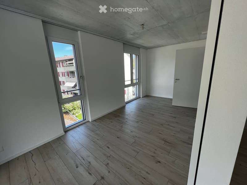 Empty room with light wooden flooring, white walls, and large windows offering a view of the outside. No furniture or equipment is present.