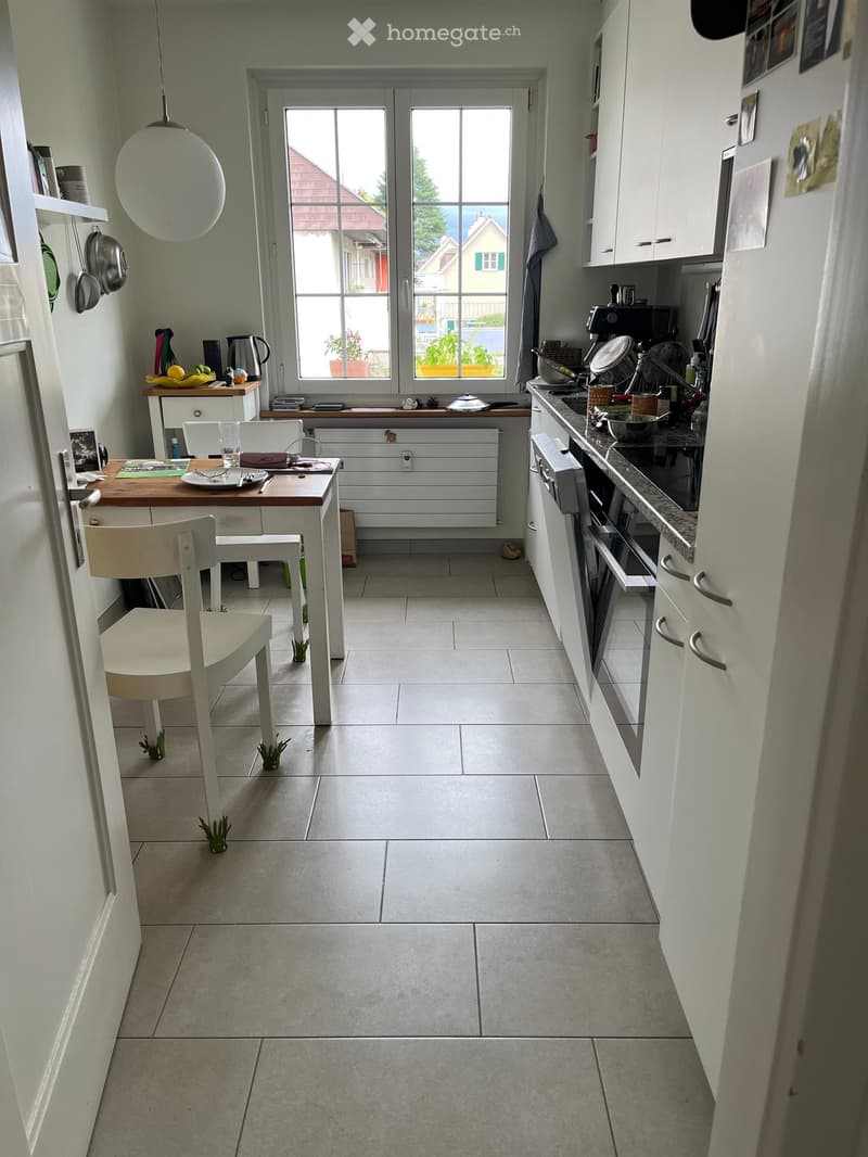Bright kitchen with white cabinets, tiled floor, and a dining area. Features include a table with chairs, a pendant light, and various kitchen appliances.