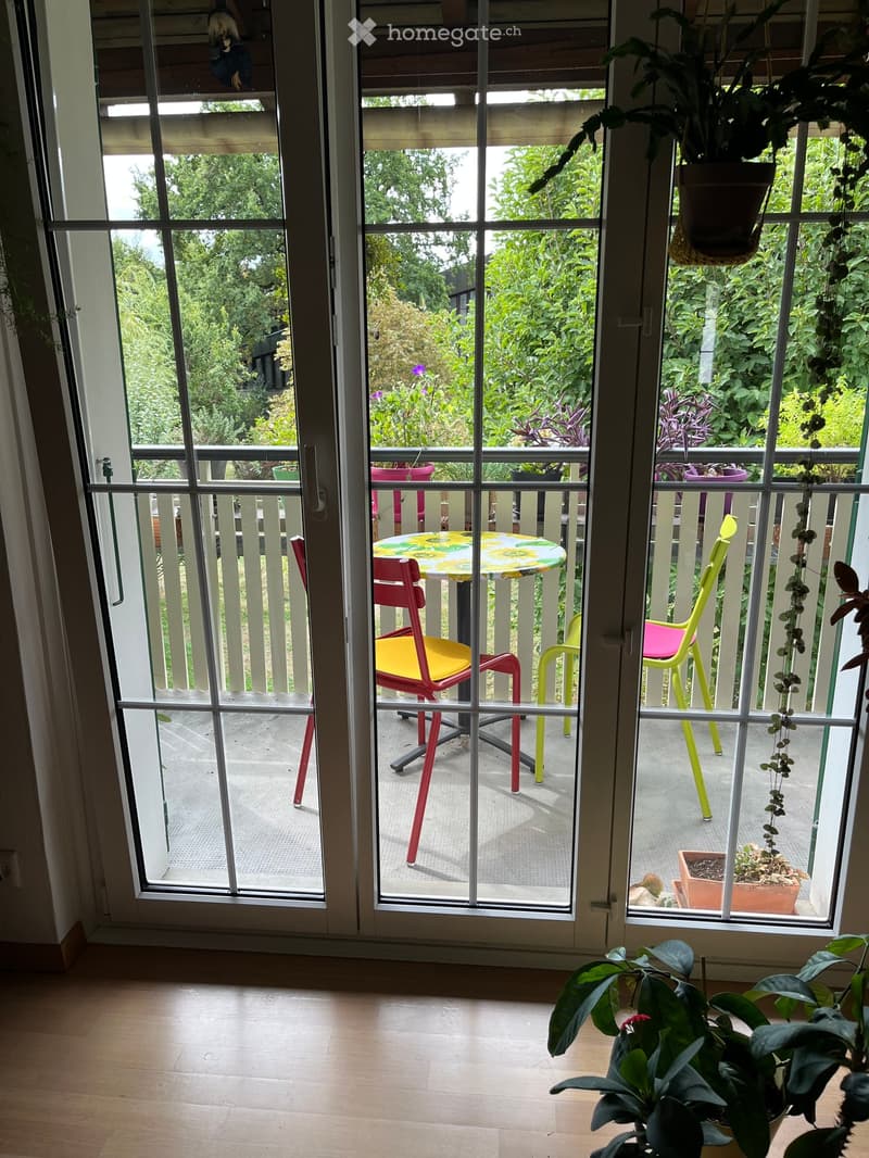 Balcony with a small table and colorful chairs, surrounded by lush greenery and potted plants.