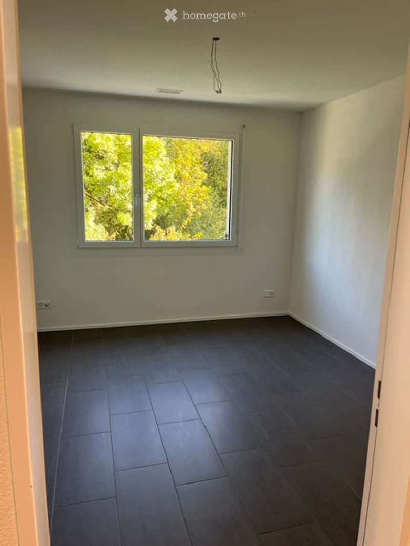 Empty room with dark tiled floor, white walls, and large window with view of greenery.