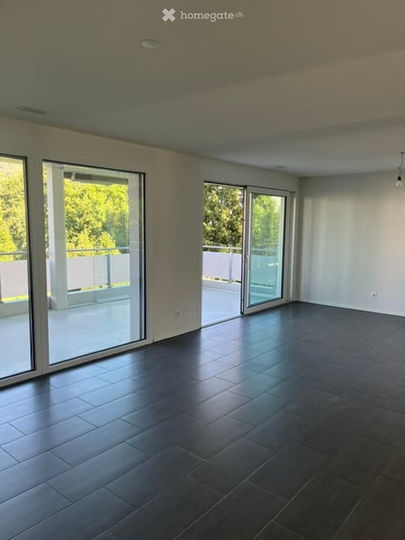 Empty room with dark wooden flooring, large glass sliding doors leading to a balcony, white walls, and recessed ceiling lighting.