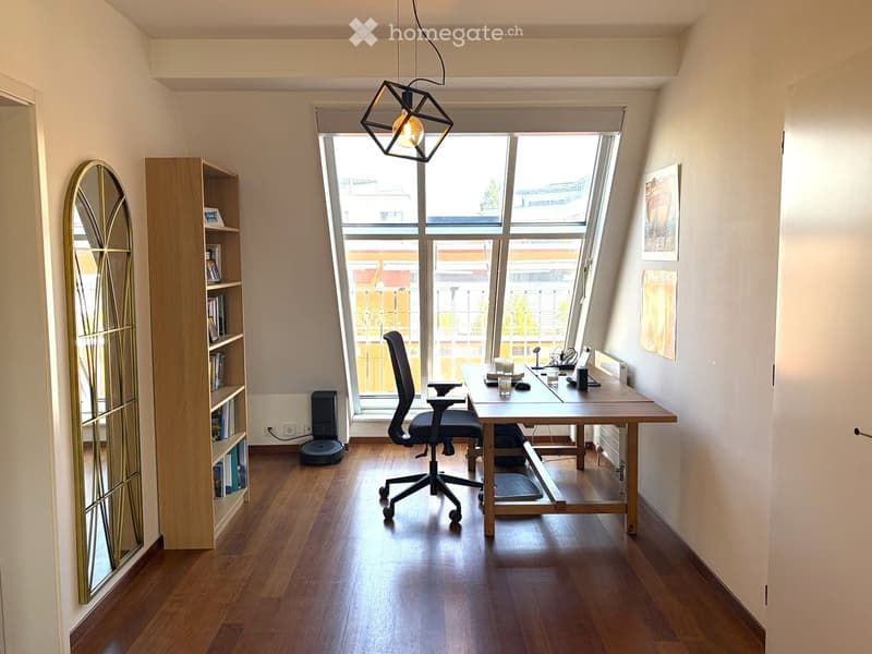 Modern, well-lit room with wooden flooring, large window, desk, ergonomic chair, bookshelf, and decorative mirror.