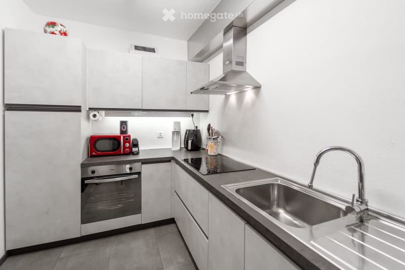 Modern kitchen with white cabinets, stainless steel appliances, and a sleek design. Features include a refrigerator, oven, microwave, sink with a modern faucet, and a range hood.
