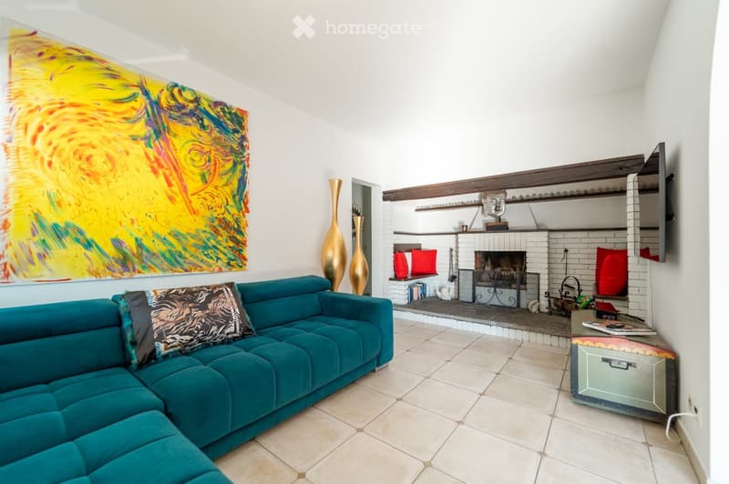 Modern living room with a teal sectional sofa, fireplace, decorative vases, and colorful artwork on the wall.