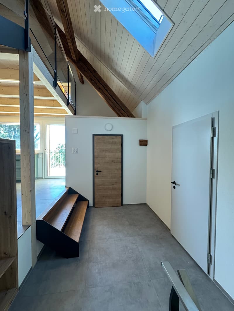 Modern hallway with wooden benches, white walls, and a skylight above. Features a wooden door and a staircase leading upwards.