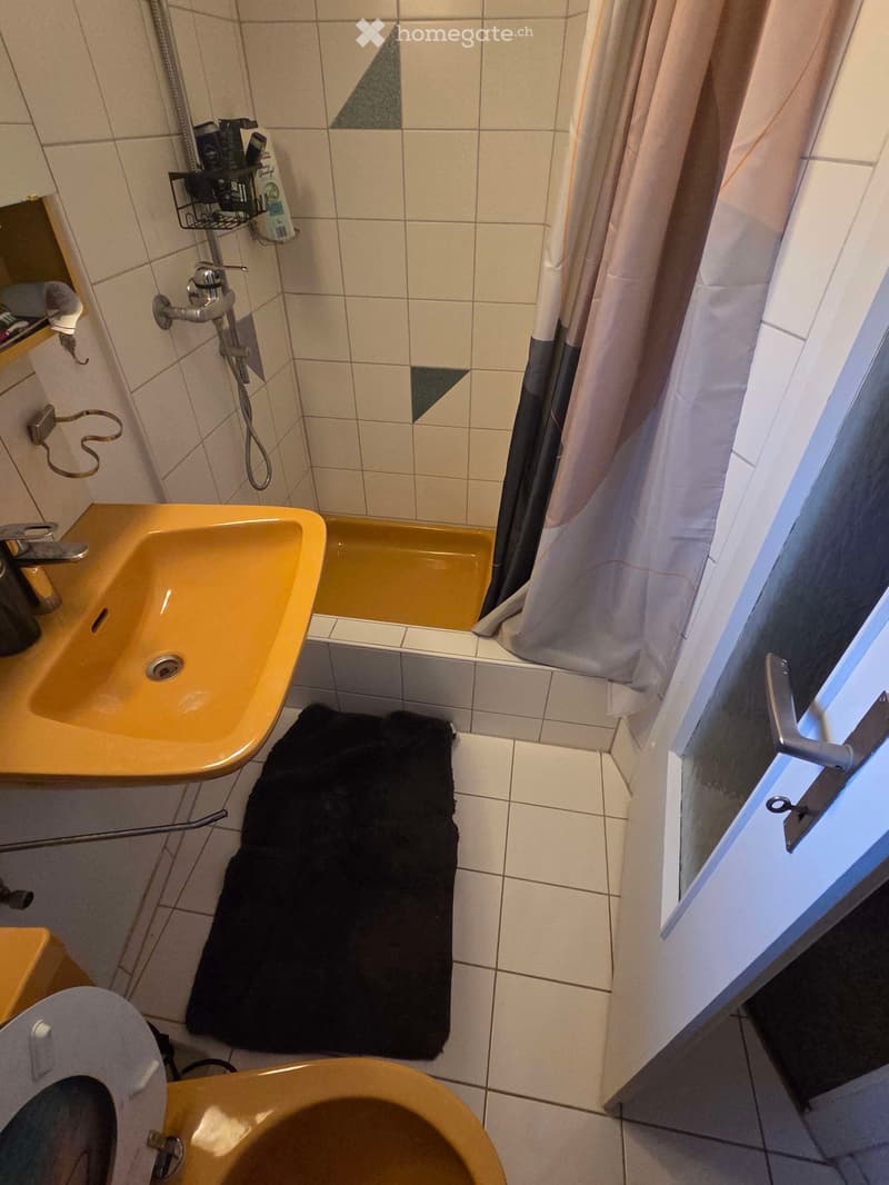 Bathroom with a yellow sink, bathtub, toilet, black towel, and shower curtain. Shower rack with toiletries is visible on the wall.