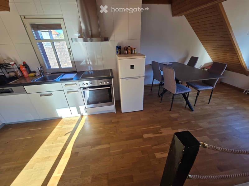 Modern kitchen with white cabinets, stainless steel appliances, wooden flooring, and a dining area with a table and chairs.