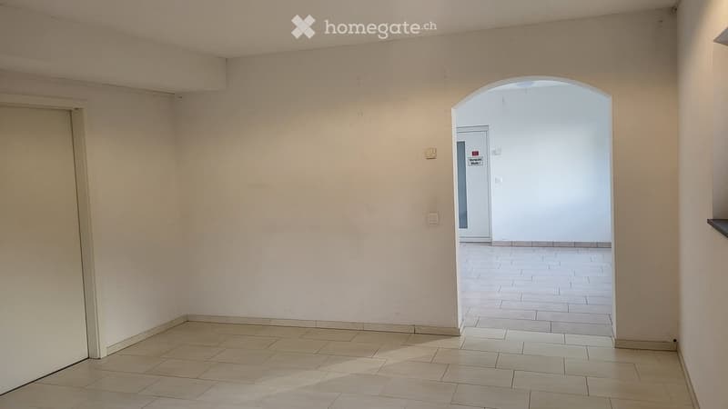 Empty room with tiled floor and beige walls, featuring an arched doorway leading to another space.