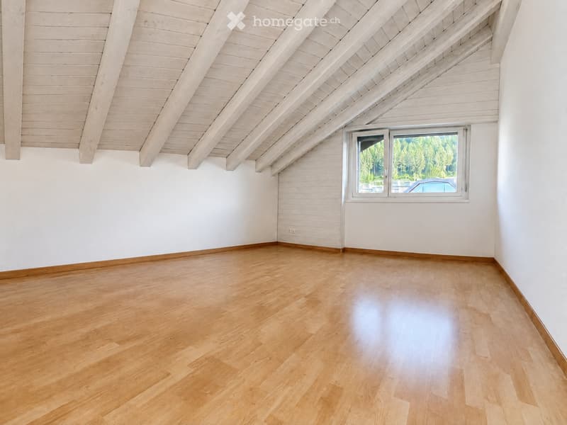 Empty room with wooden flooring, white walls, and a large window showing a view of trees and a parked car.