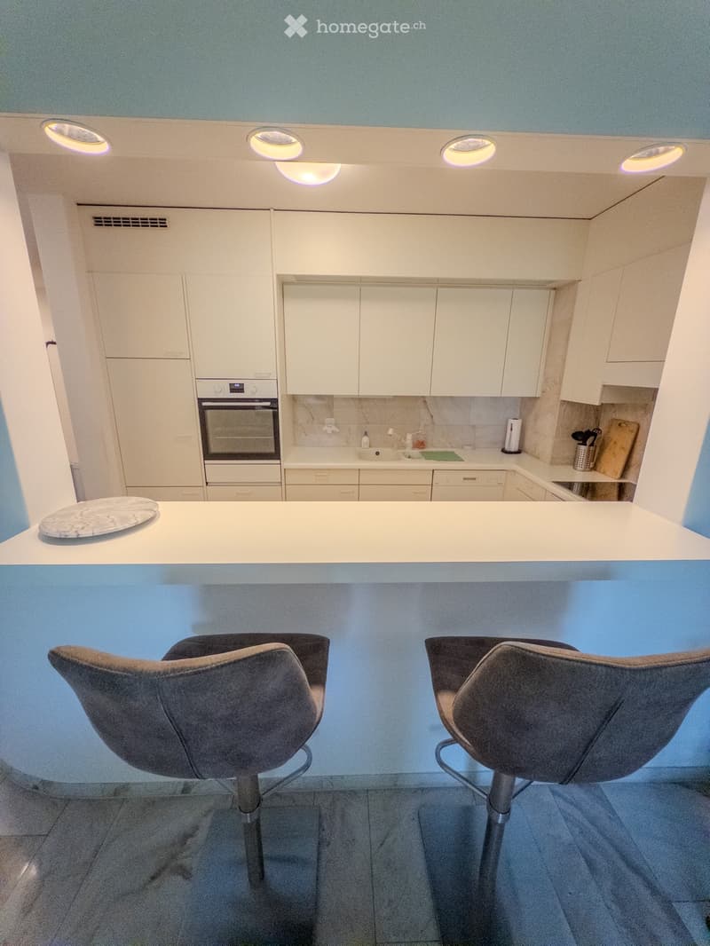 Modern kitchen with white cabinets, stainless steel appliances, and a central island with bar stools.