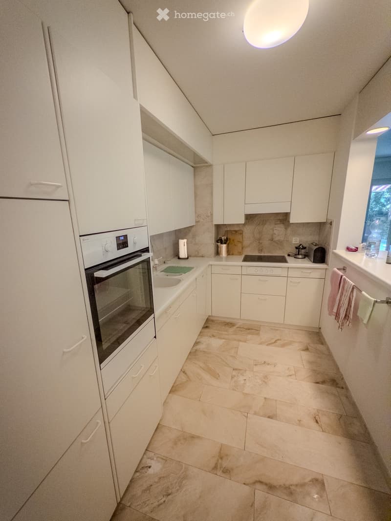 Modern kitchen with white cabinets, marble flooring, and stainless steel appliances including an oven, dishwasher, and sink.