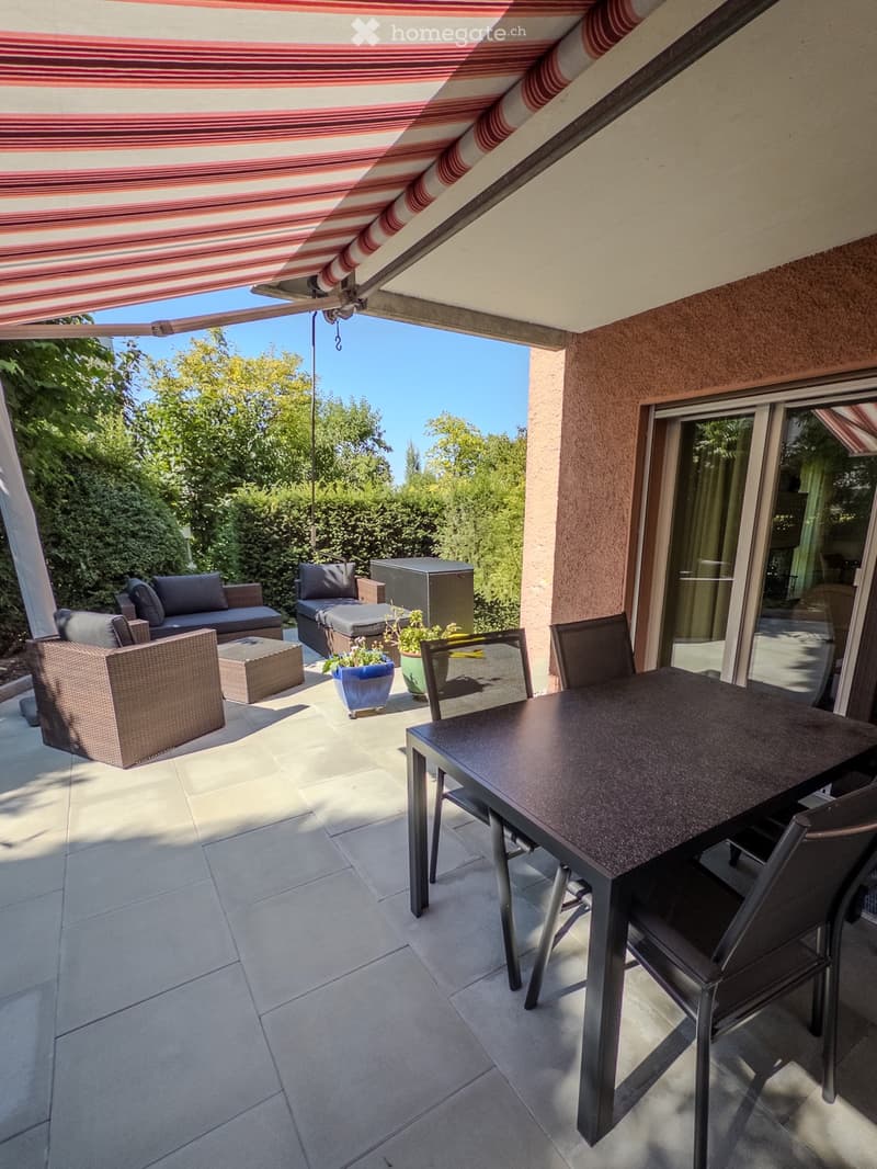 A covered outdoor patio with a tiled floor, a sofa, chairs, a dining table, and potted plants.