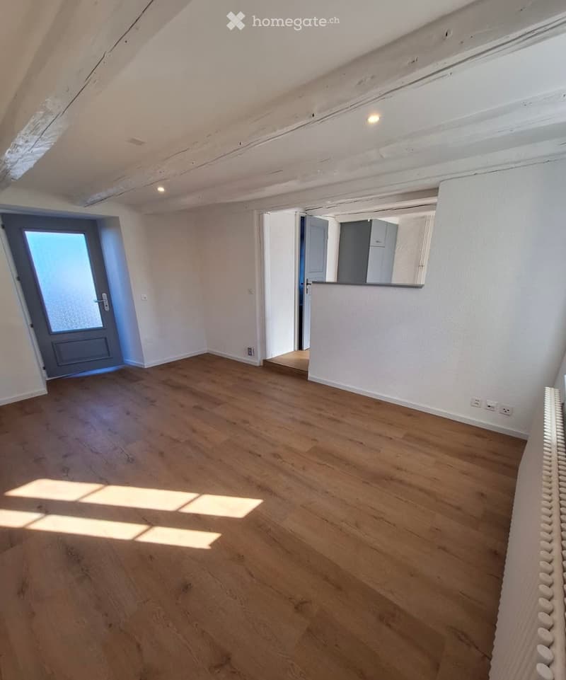 Empty room with wooden flooring, white walls, and a door leading to another space. No furniture or equipment is present.
