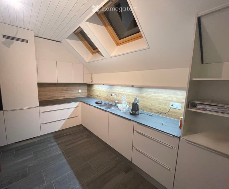 Modern kitchen with light-colored cabinets, dark countertops, and a dark tiled floor. Features include a sink, faucet, and small appliances on the counter.