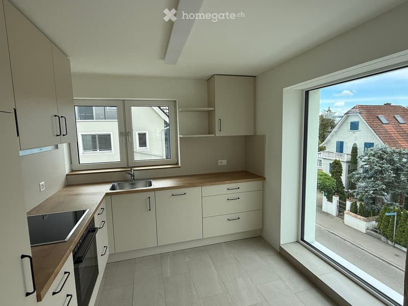 Modern kitchen with light-colored cabinets, wooden countertops, and stainless steel sink and oven. Large window offers a view of the neighborhood.