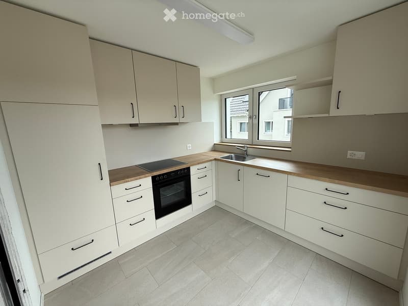 Modern kitchen with light-colored cabinets, wooden countertops, and built-in appliances including an oven and induction cooktop. Features a sink with a modern faucet and large windows offering a view of the exterior.