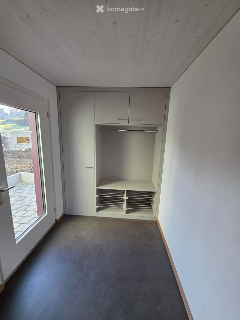 Unfurnished Room. Empty room with light-colored walls, carpeted floor, built-in closet with shelves and hanging space, and a large window with a view of the outdoors.
