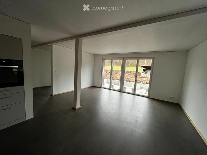Unfurnished Room. Empty room with grey walls, dark grey floor, large sliding glass doors leading to outdoor area, and a built-in cabinet with drawers on the left side.