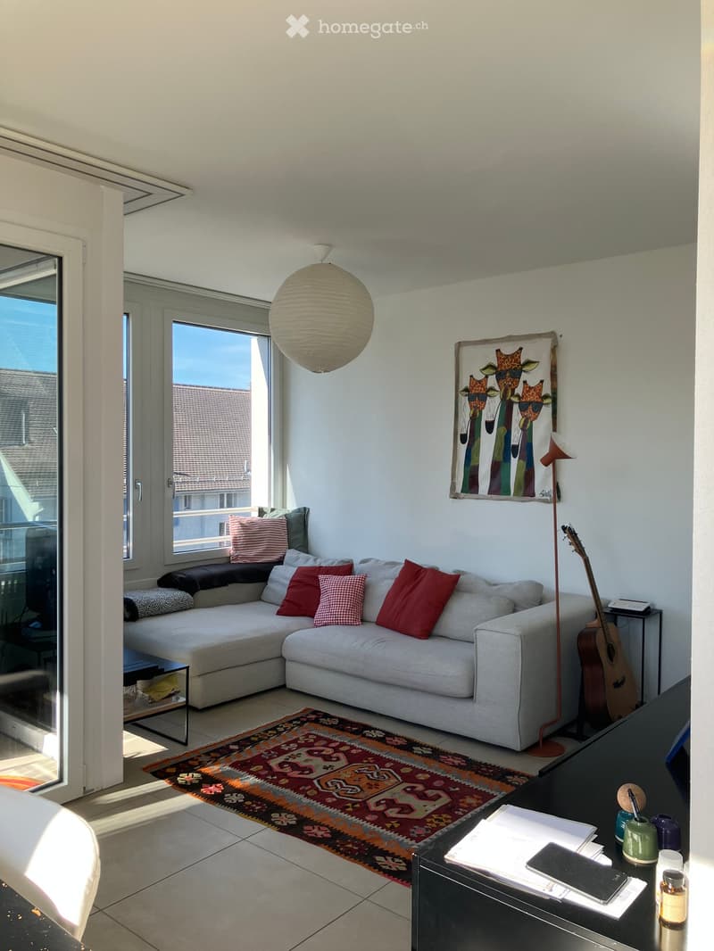 Modern living room with a grey sectional sofa, colorful pillows, a coffee table, a floor lamp, a guitar, and a colorful rug.
