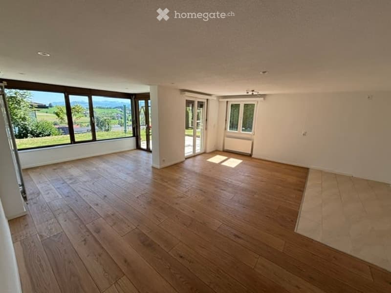 Completely empty room with wooden flooring, large windows, and a sliding glass door leading to an outdoor area.