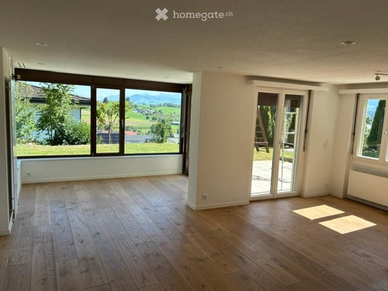 Bright, empty room with wooden flooring and large windows offering a scenic view of the countryside.