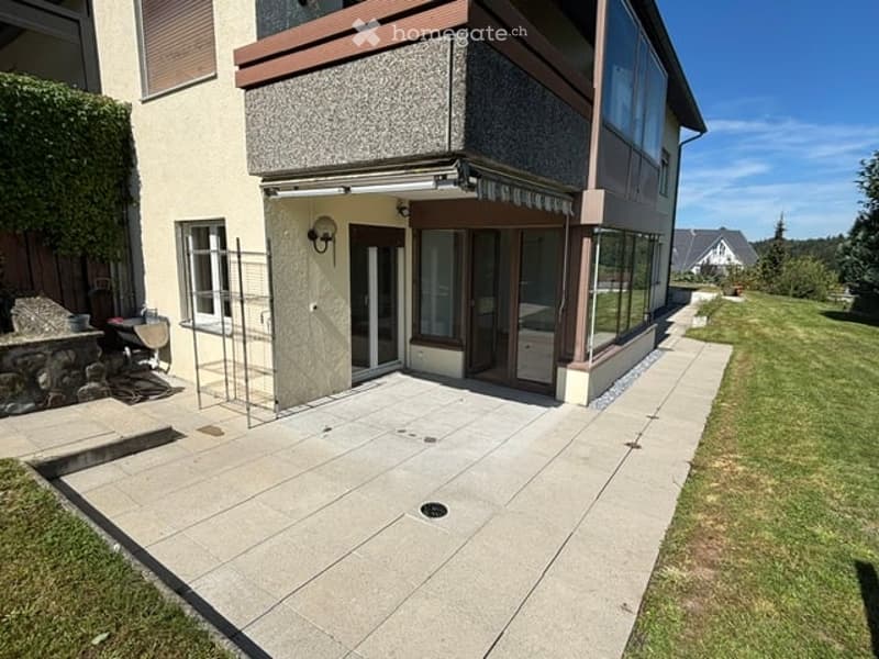 Modern house exterior with a paved patio, large windows, and a well-maintained lawn.