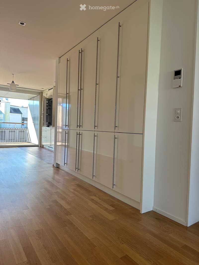 Modern kitchen with light-colored cabinets, wooden flooring, and a large window leading to a balcony.