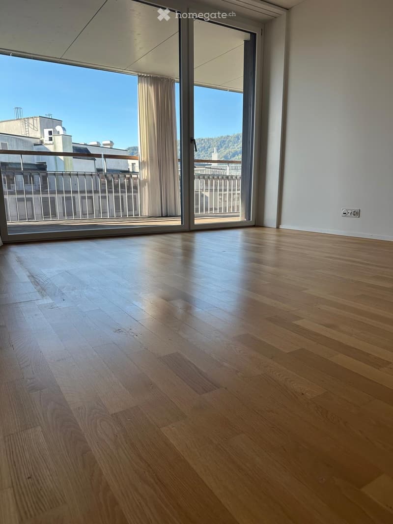 Empty room with wooden flooring, large sliding glass doors leading to a balcony with a city view.