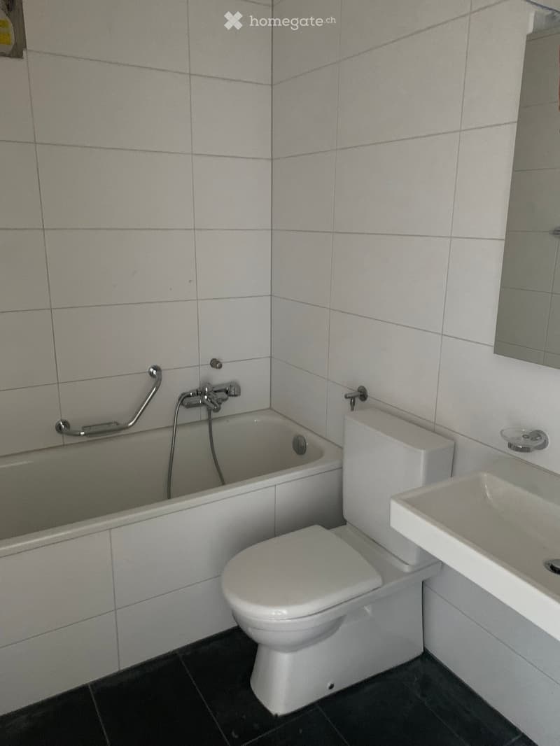 A small bathroom with white tiled walls and black tiled floor, featuring a toilet, bathtub, and sink.